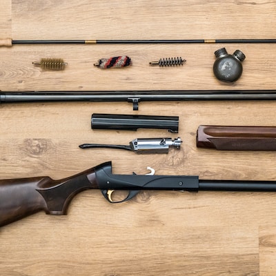 disassembled shotgun parts and cleaning kit on the wooden background